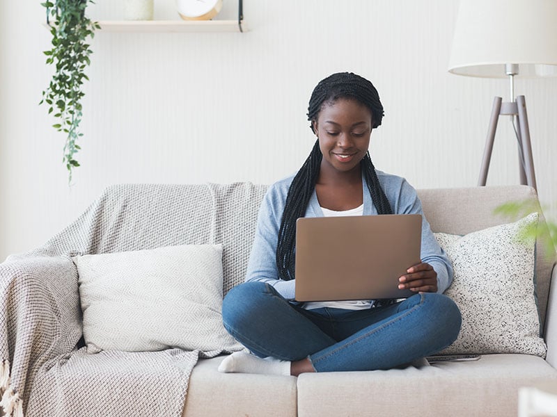 Black-millennial-woman-working-with-laptop-computer-on-sofa-at-home